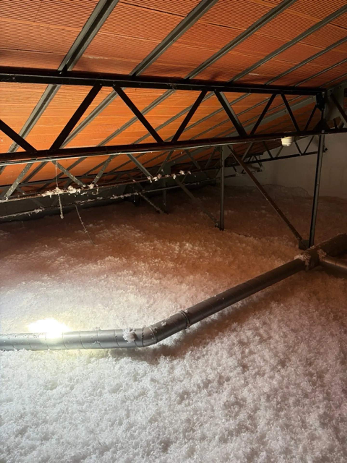 Isolant blanc nivelé dans les combles, sous la ferme métallique de la toiture